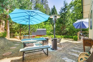 Eine Terrasse im Freien mit Picknicktischen, einem Grill und Sonnenschirmen.