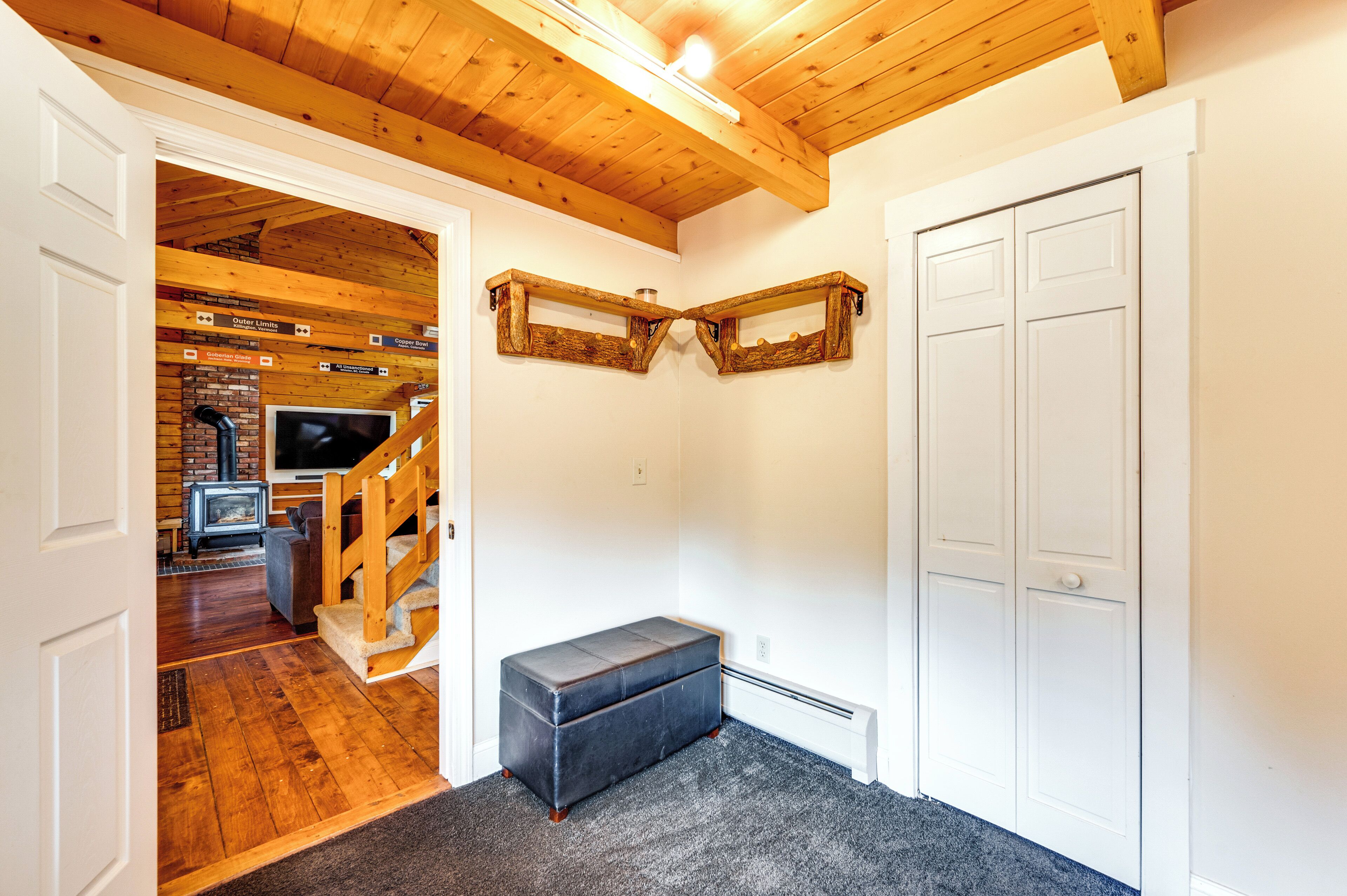 A room with a wooden ceiling, a bench, a white door, and a brick wall with a fireplace.