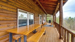 Eine Holzterrasse mit Holztisch und -bänken, mit Blick auf ein bewaldetes Gebiet.