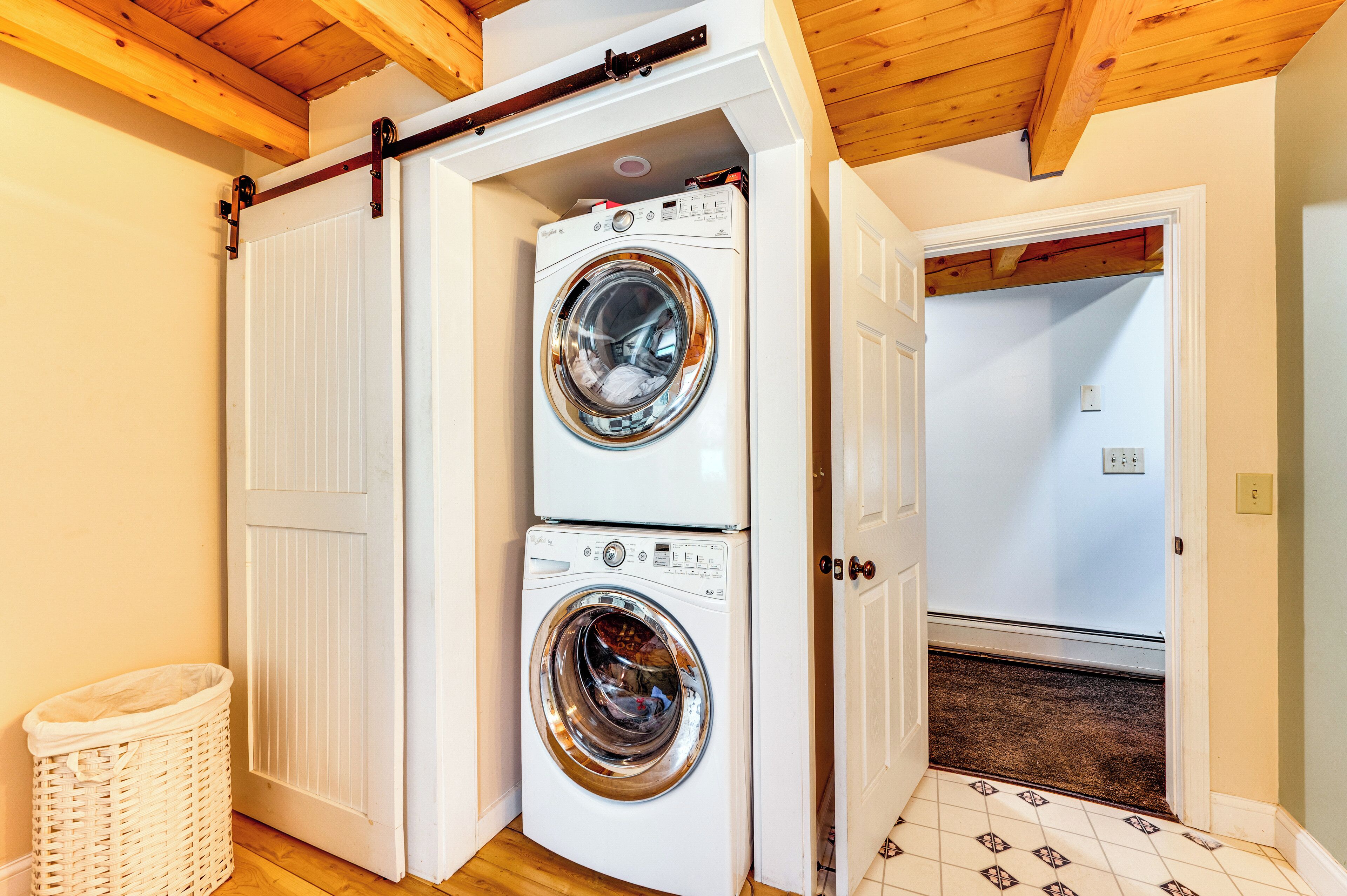 A laundry room with two stacked front-loading washing machines, a white wicker laundry basket, and a tiled floor.