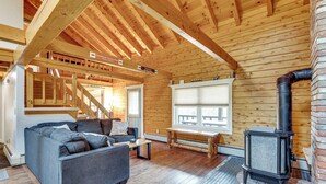 Ein gemütliches Blockhaus-Interieur mit Holzbalkendecke, einer Couch, einer Bank und einem Kaminofen.