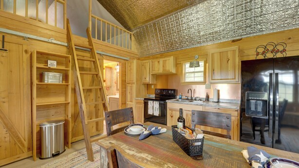 Una cocina rústica con armarios de madera, un refrigerador de acero inoxidable y una mesa de madera preparada para comer.