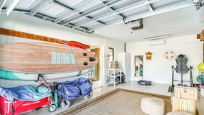 Un garage où l’on trouve une planche de surf, une poussette et une guitare.