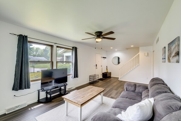 A spacious living room with a flat-screen TV, a wooden coffee table, a gray sofa, and a ceiling fan.