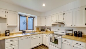 A modern kitchen with white cabinets, a wooden countertop, a built-in oven, a microwave, and a coffee maker.