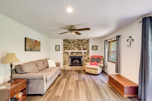 A living room with a fireplace, a sofa, a chair, a lamp, and a ceiling fan.