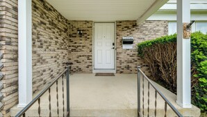 A brick house with a white door, a small porch, and a metal railing.