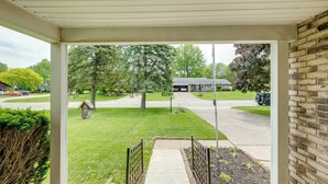 A covered porch with a view of a suburban street, a small garden, and a mailbox.