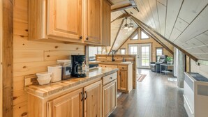 A spacious kitchen with wooden cabinets and a large island, a dining area with a table and chairs, and a view of the outdoors through large windows. - 1/2 Mi to Ruby River: Cabin w/ Trail Access! (Alder)