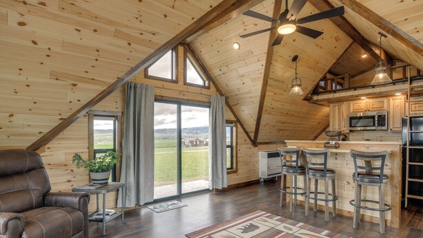 A spacious loft with a high ceiling, wooden beams, a large window, a kitchen with bar stools, and a leather recliner. - 1/2 Mi to Ruby River: Cabin w/ Trail Access! (Alder)