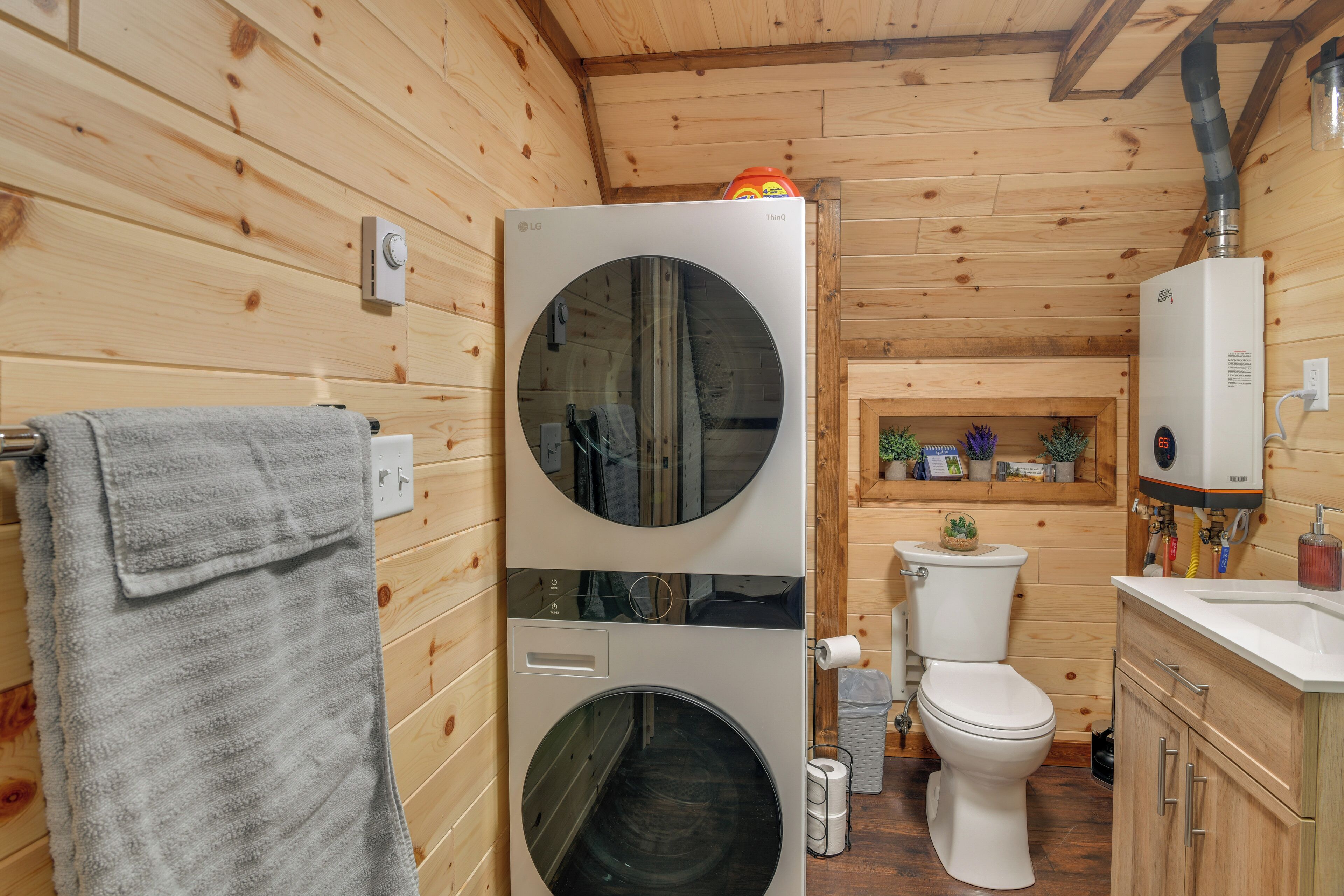 Een klein, houten badkamertje in chaletstijl met een voorlader wasmachine, toilet en wastafel.