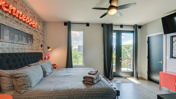 A modern bedroom with a large bed, a ceiling fan, a cityscape poster, and a neon sign. - Skyline Views: Nashville Townhome 3 Mi to Broadway (Nashville)