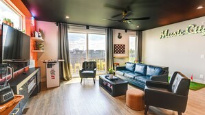 A modern living room with a black leather sofa, a coffee table, and a TV on a wooden stand. There is a balcony with a view of the city. - Skyline Views: Nashville Townhome 3 Mi to Broadway (Nashville)