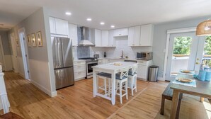 Una cocina moderna con armarios blancos, electrodomésticos de acero inoxidable y un comedor con mesa y sillas.