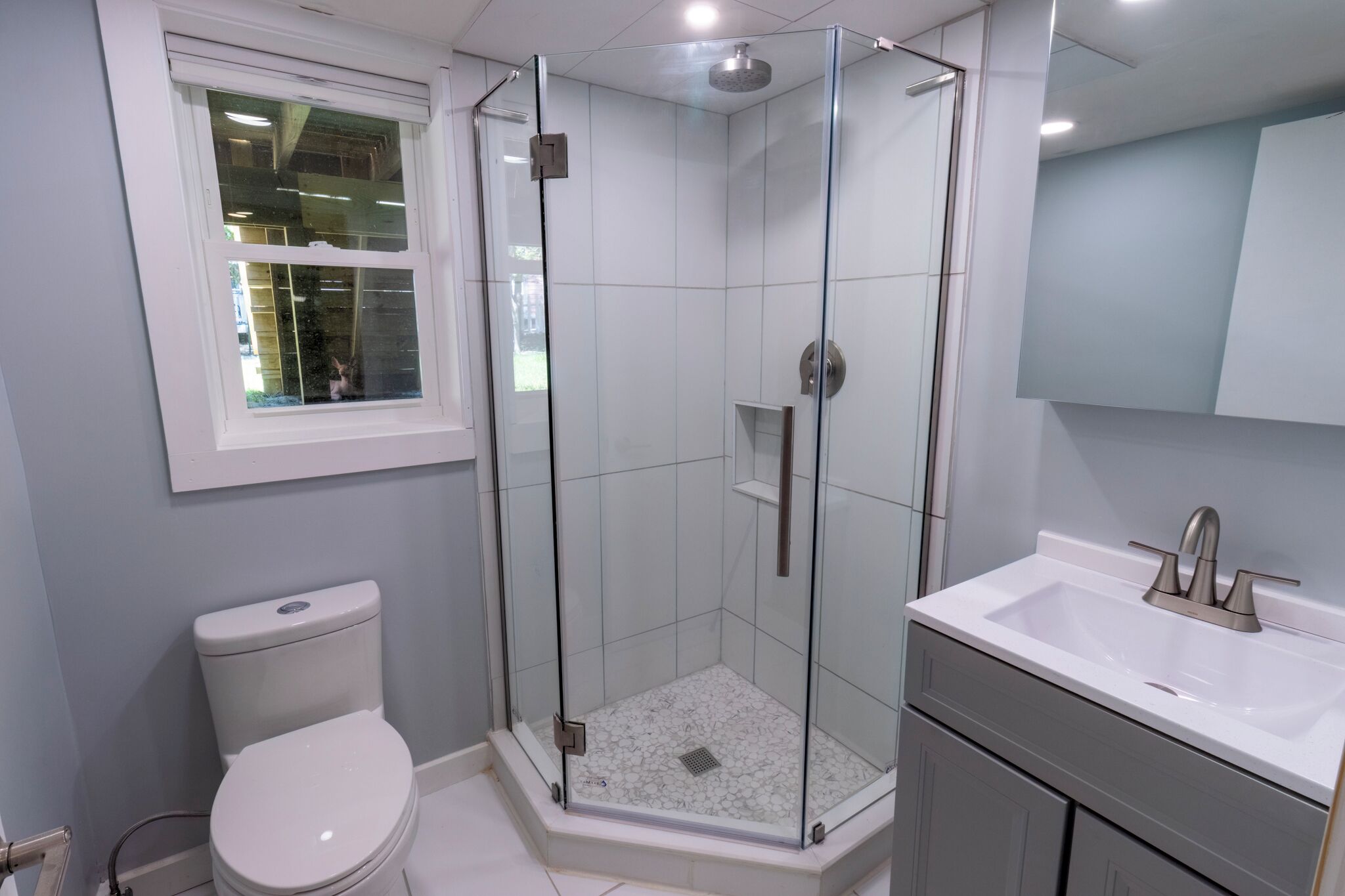 A modern bathroom with a glass-enclosed shower, a white toilet, and a sink with a mirror above.