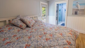 Un dormitorio con una colcha de estampado floral, un cabecero blanco y un cuadro de un pájaro en la pared.