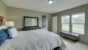 A bedroom with a large bed, a bench, a mirror, and a window with a view of a green field. - Family-friendly Home w/ Pond, 5 Mi to Splashway! (Rock Island)