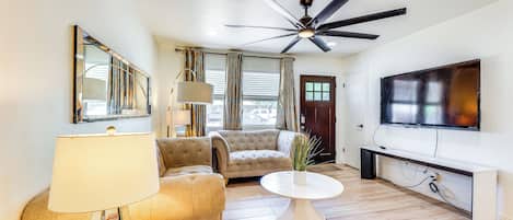 A living room with a ceiling fan, a sofa, a coffee table, a lamp, and a TV mounted on the wall.