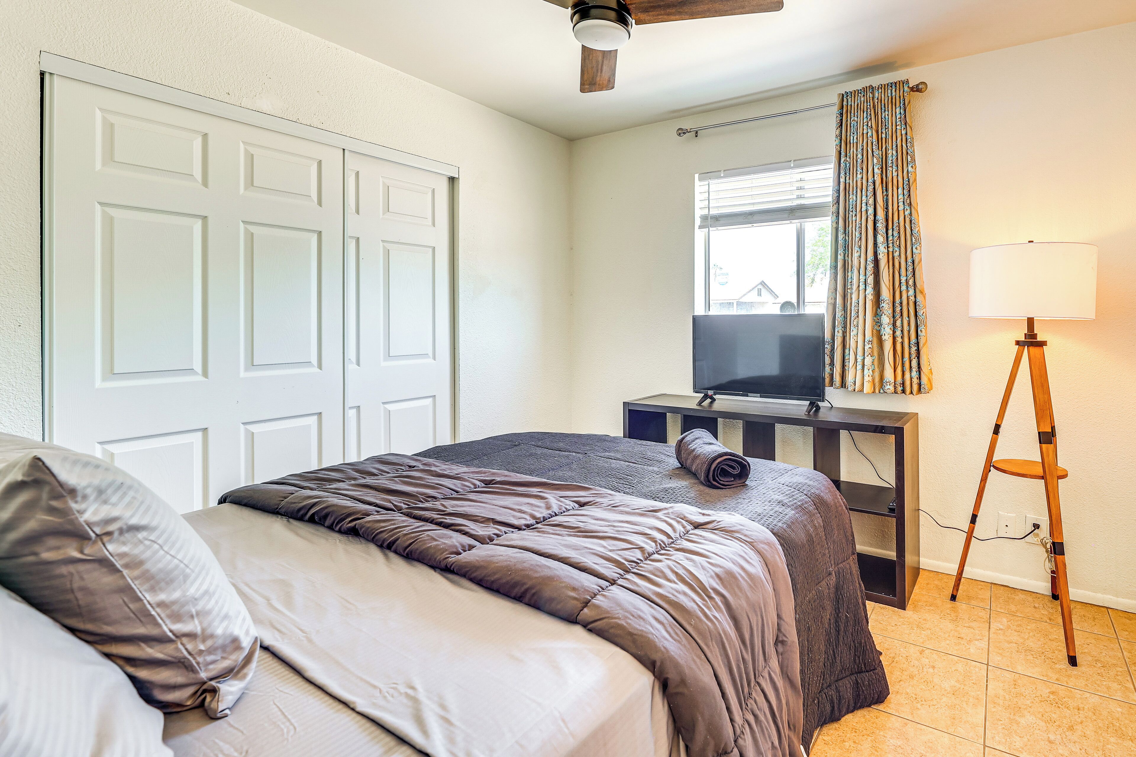 A bedroom with a bed, a desk with a television, a lamp, and a window with curtains.