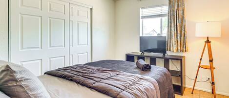 A bedroom with a bed, a desk with a television, a lamp, and a window with curtains.