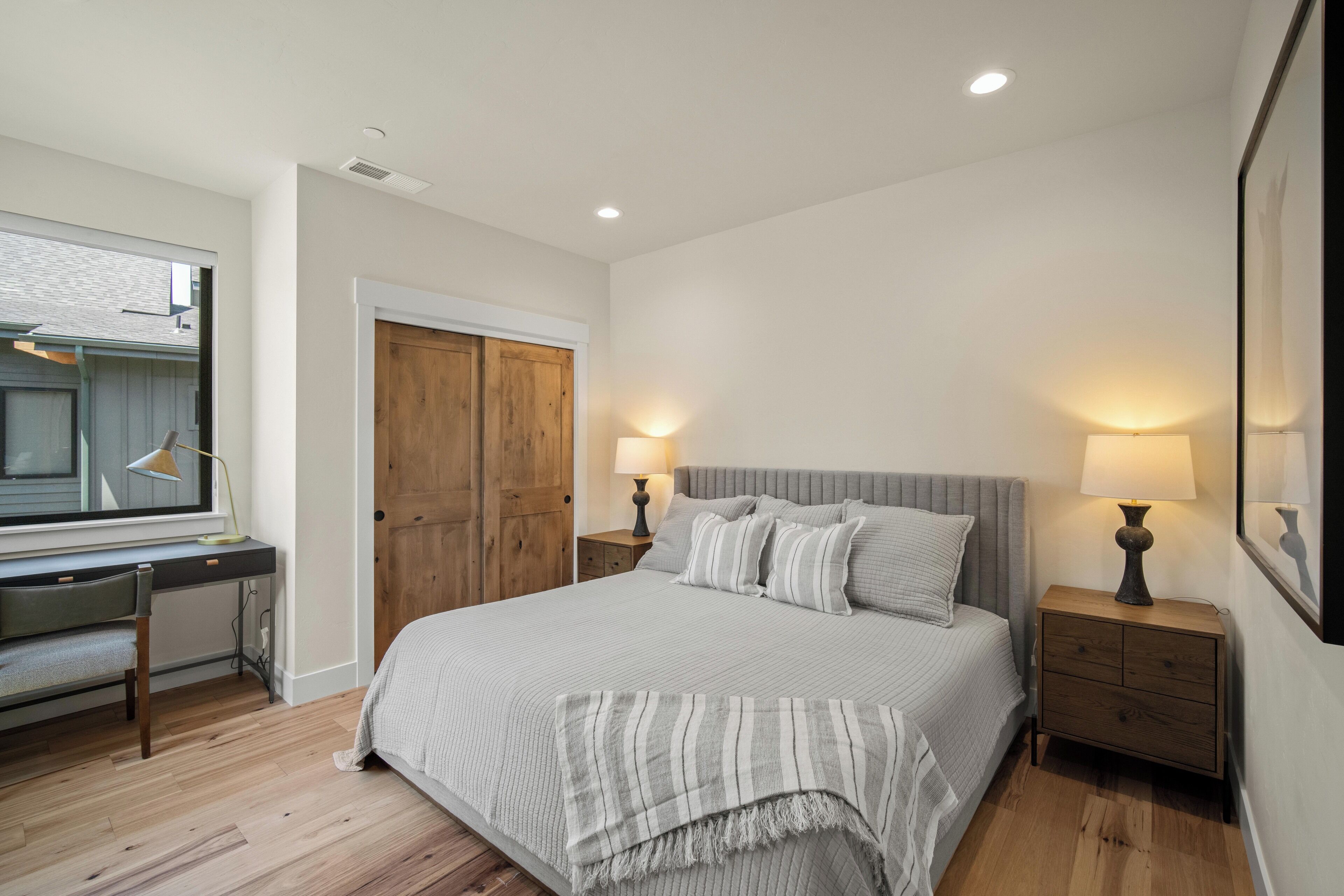 A bedroom with a bed, bedside tables, a desk, and a window.