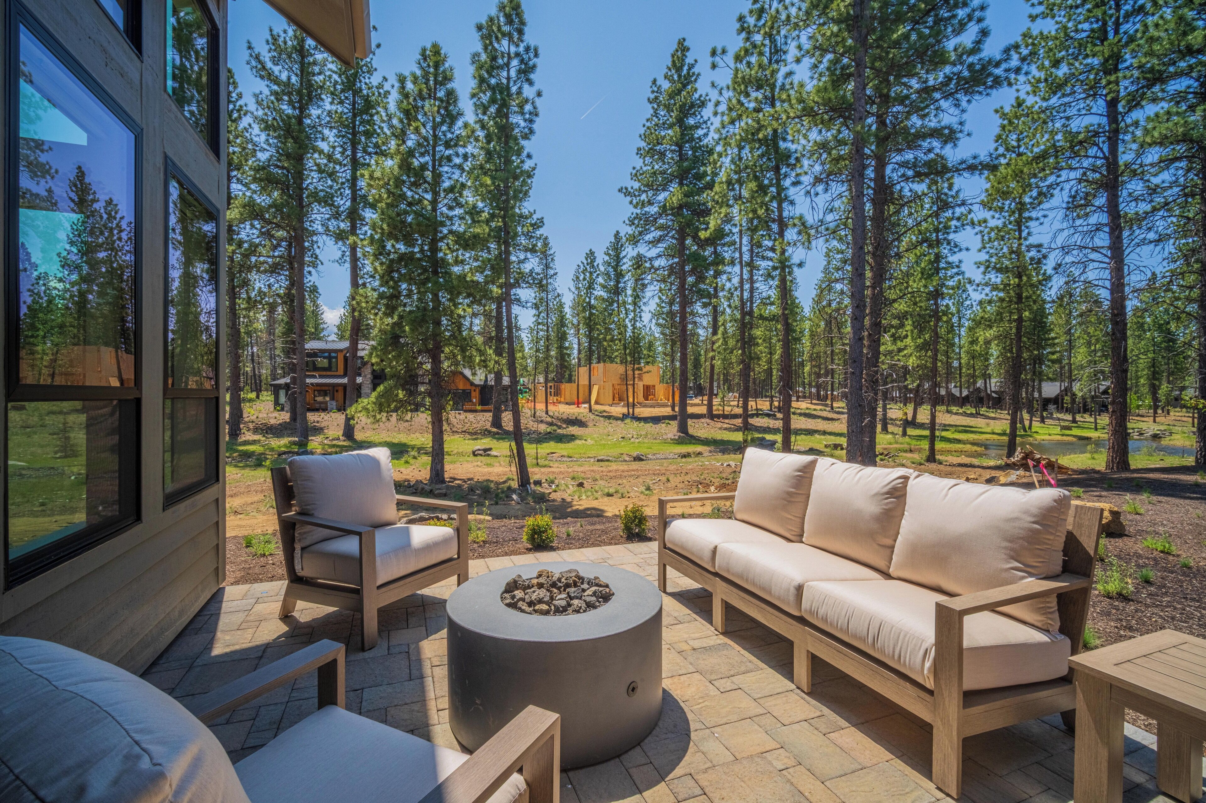An outdoor patio with a sofa, chairs, and a round table, surrounded by a forested area.