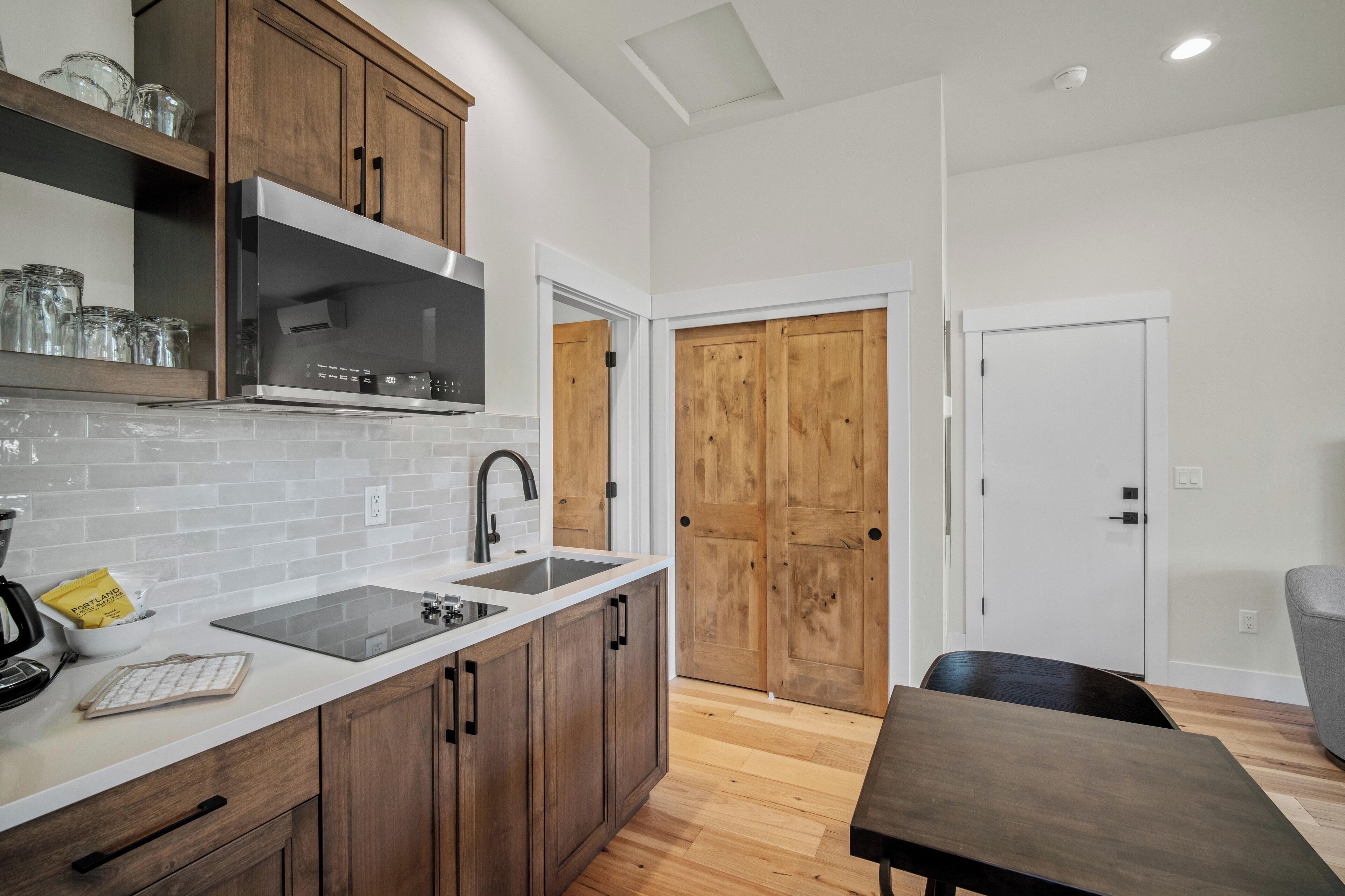 A modern kitchen with wooden cabinets, a stainless steel range hood, a double sink, and a dining area with a table and chairs.