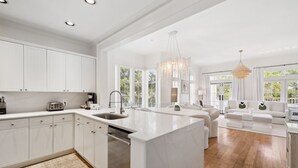 Una cocina amplia con armarios blancos, una isla grande y una zona de comedor con un sofá blanco.