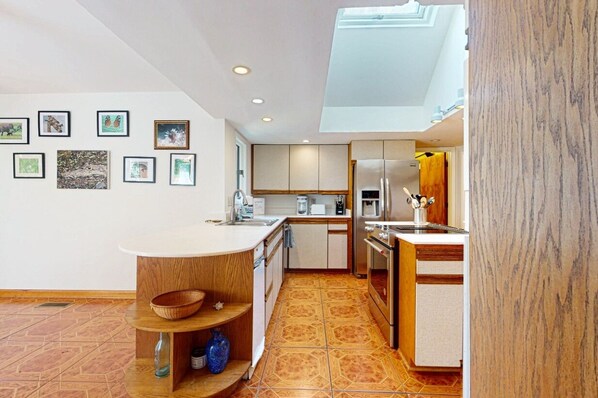 A modern kitchen with a central island, wooden cabinets, and a skylight.