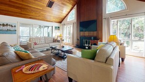 Un salón espacioso con techo alto, ventanas grandes, chimenea y televisor.