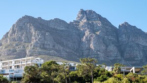 Una montaña con cima rocosa y un edificio blanco con varios balcones en primer plano.