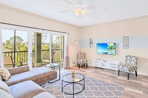 A spacious living room with a balcony, a ceiling fan, a flat-screen TV, and a white entertainment unit.