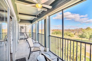 A covered balcony with a ceiling fan, large windows, and outdoor seating.
