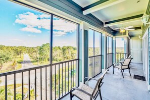 A balcony with large windows, a ceiling fan, and two chairs.