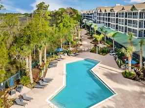 Een hotel met een groot zwembad, omringd door ligbedden en palmbomen.