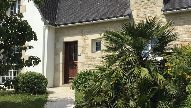 Une maison à deux étages avec une façade en pierre, un toit sombre et une porte d’entrée.