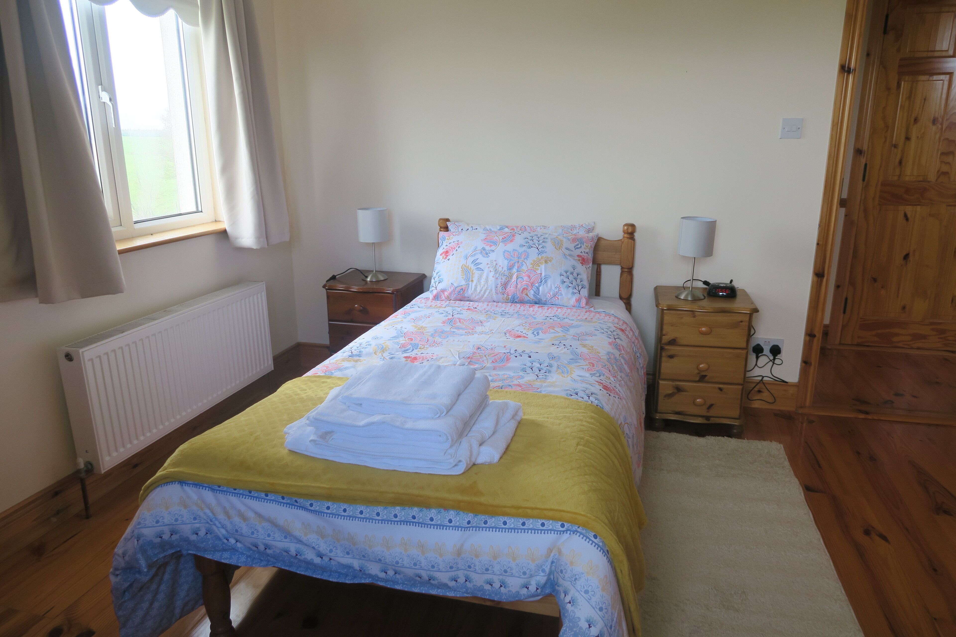 Un dormitorio con cama, dos mesitas de noche, un armario de madera, un radiador y una ventana con cortinas.
