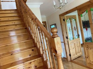 A wooden staircase with a balustrade, a chandelier, and a stained glass door. - Burkes Holiday Cottages (Rathnamagh)