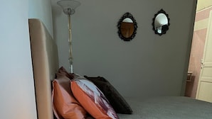 Un dormitorio con una cama, almohadas, una lámpara de noche y una mesita con lámpara.