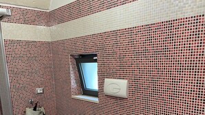 Ein Badezimmer mit roten und weißen Mosaikfliesen, einer weißen Toilette, einem Bidet, einem kleinen Fenster und einem Handtuchhalter.