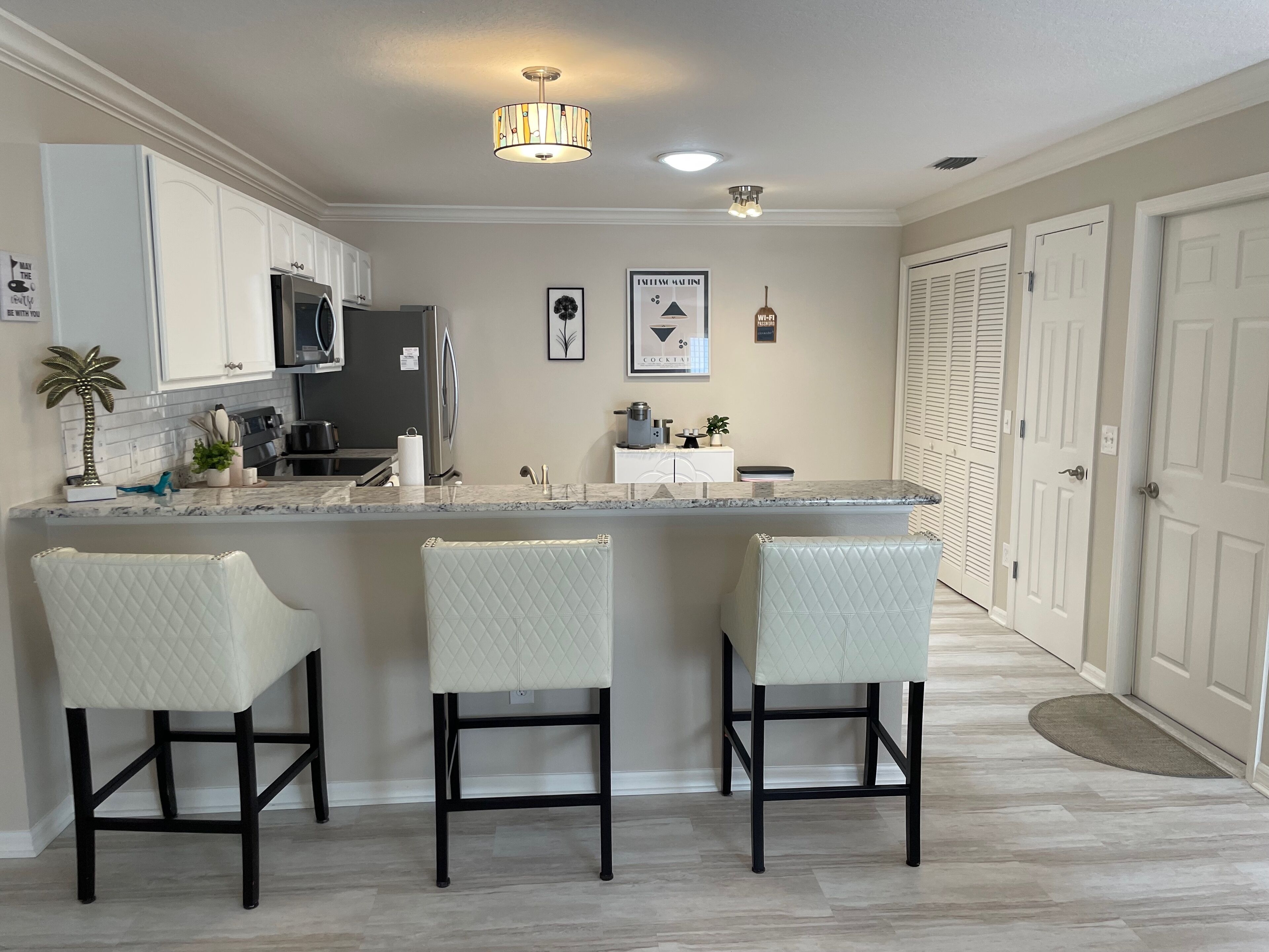 A kitchen with a central island, white bar stools, and a refrigerator.