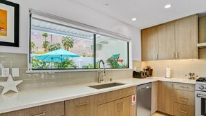 A modern kitchen with wooden cabinets, a stainless steel sink, and a window overlooking a garden. - The Cove: Heated Pool, BBQ, Walk To Downtown PS (Palm Springs)