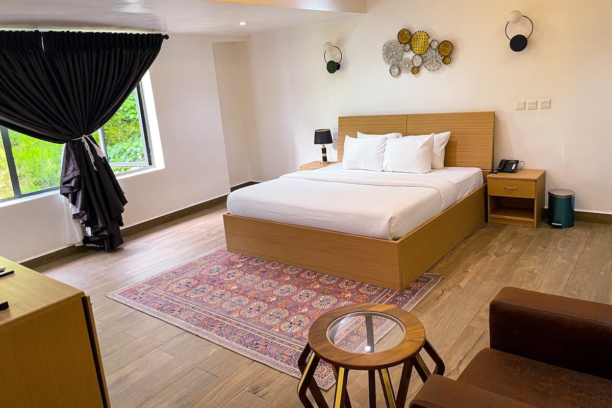 Quarto moderno com cama de madeira, mesas de cabeceira, uma pequena mesa redonda e um tapete estampado.