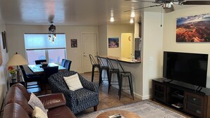 A living room with a sofa, a coffee table, a TV, a ceiling fan, a dining area with chairs, and a kitchen area with a refrigerator. - 17A3 Two Master Suites, Views, Community Pool & Hot Tub (Moab)