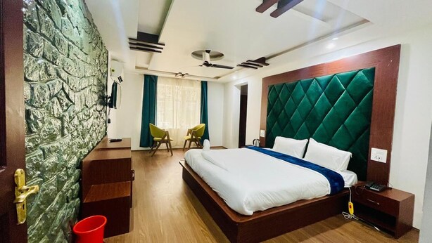Habitación de hotel con una cama grande, un cabecero tapizado en verde, una mesita de noche de madera, un cubo rojo y un equipo de aire acondicionado instalado en la pared.
