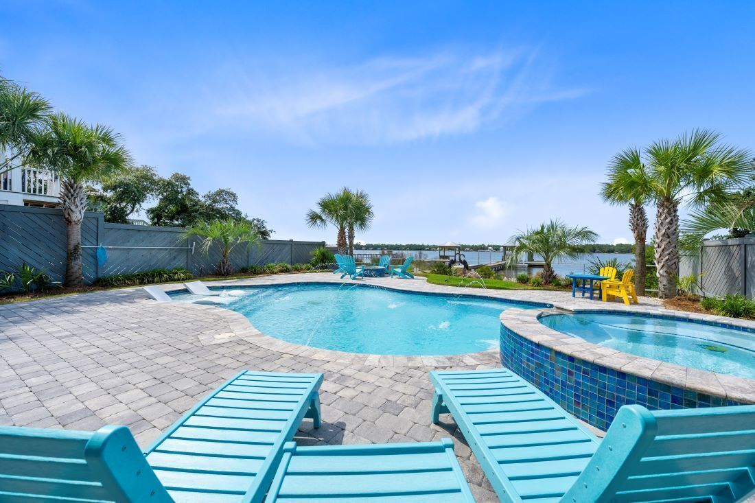 A swimming pool with blue lounge chairs, a small table, and palm trees.