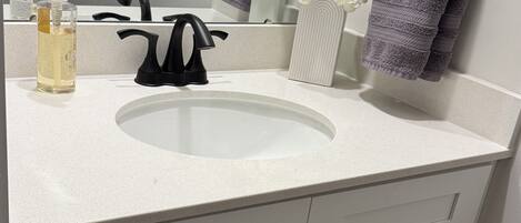 A bathroom with a white sink, black faucet, and two towels hanging on hooks. There is a bottle of hand soap and a vase with white flowers on the counter.