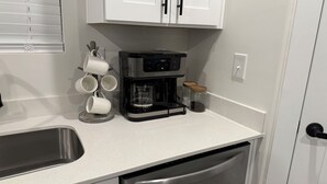 A kitchen with a coffee maker, a mug holder, a jar, and a dishwasher.