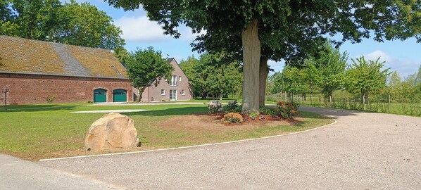 A brick building with a green door, a large tree, and a paved driveway. - Coproyshof Lakeside Apartment (Wesel)