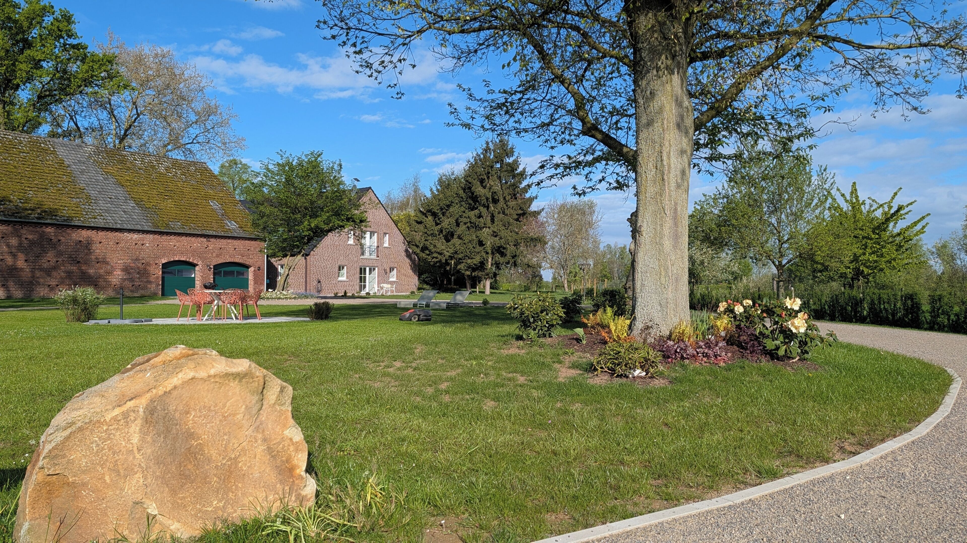 A brick building with a green door, a lawn with a large rock, and a tree.